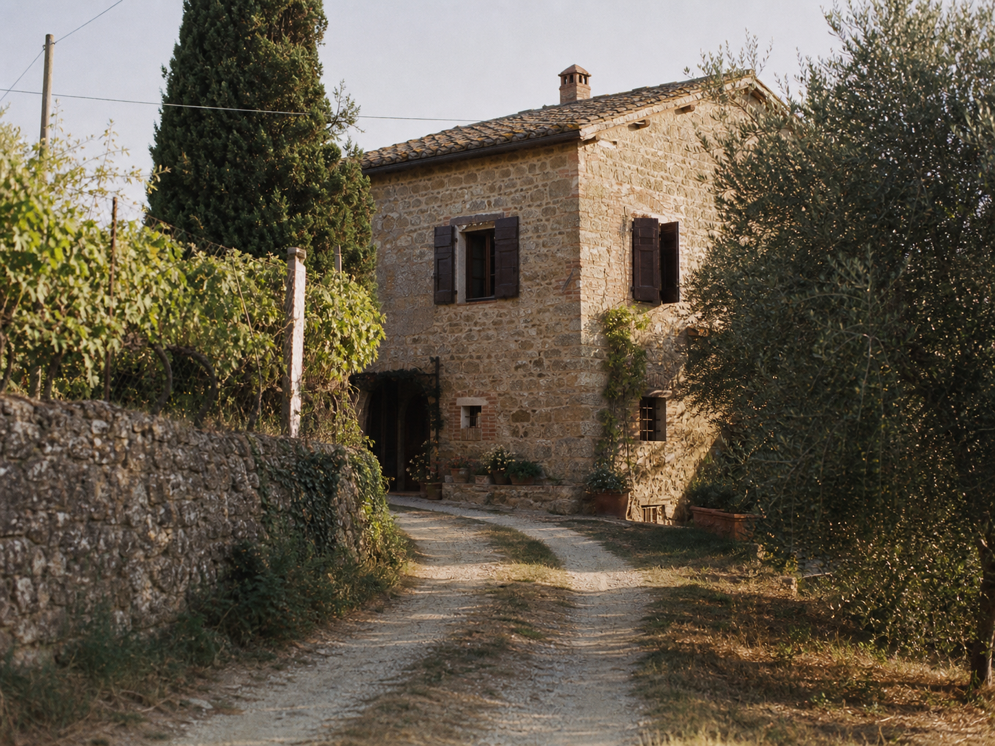 Facciata in pietra del casale toscano con vialetto di ghiaia e alberi